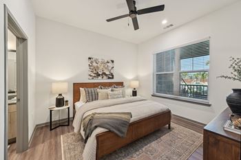 A bedroom with a large bed, a ceiling fan, and a window with blinds.